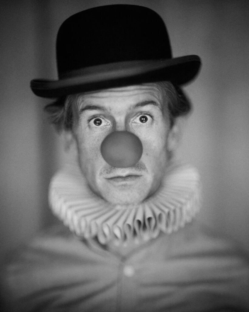 Black and Grey Self Portrait of man with bowler hat, clown ball nose, neck ruff. 2021 British Photography Awards. Guy Bellingham Portrait Photographer, Professional Photographer, Celebrity Photographer, Fine Art Photographer, tintype.